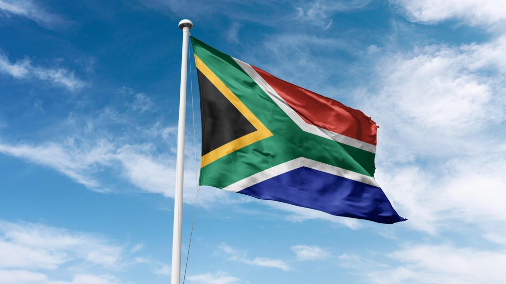 Drapeau de l'Afrique du Sud ayant comme fond un ciel bleu avec des nuages.